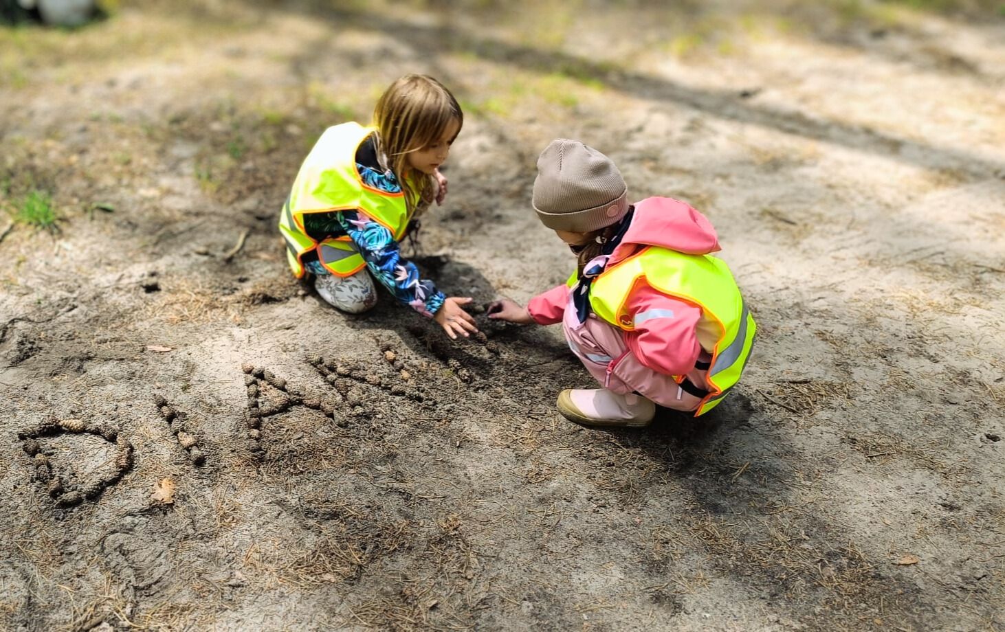 Dzieci podczas zajęć outdoorowych w lesie uczą się przez zabawę, tworząc napisy z naturalnych materiałów.